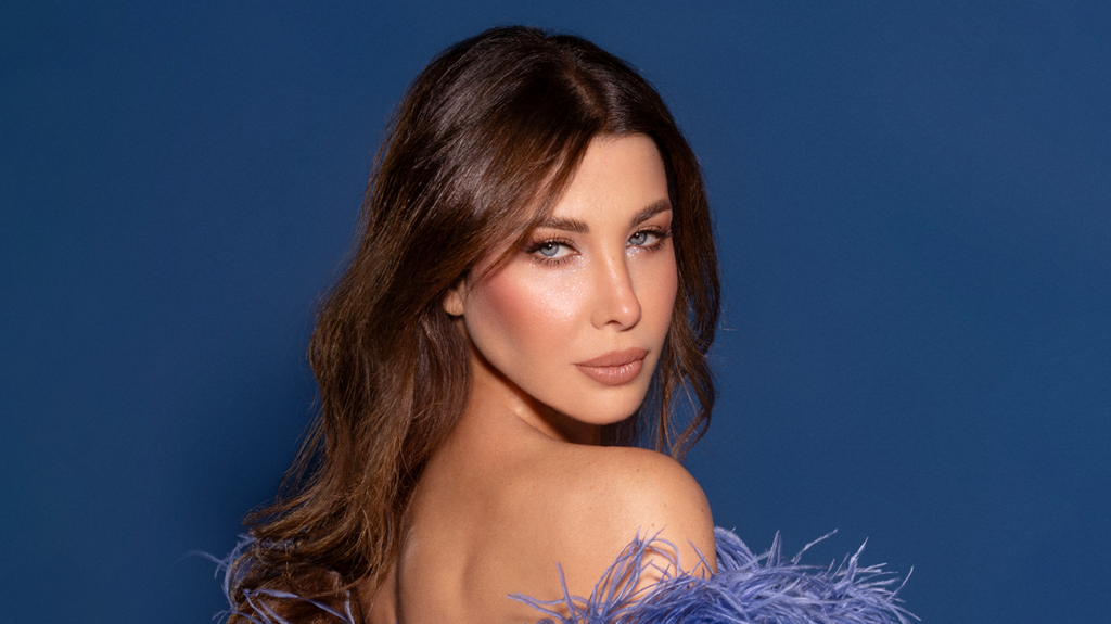 Singer Nancy Ajram posing in a blue dress against a blue background.